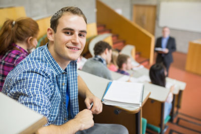 Portrait of a smiling male with students and teacher at the college lecture hall