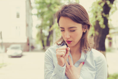 Young woman having asthma attack or choking can't breath suffering from respiration problems standing outdoors on a urban street