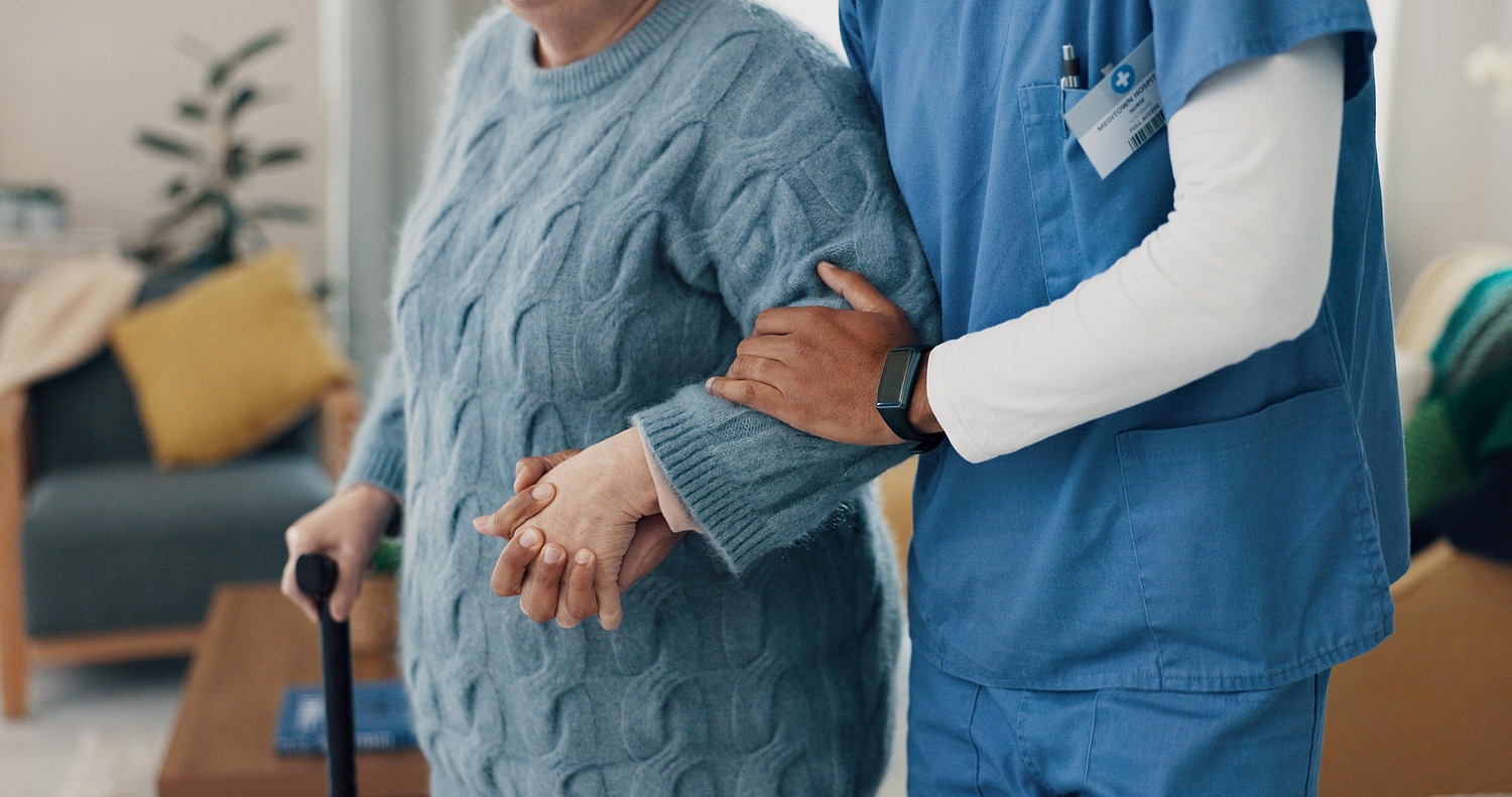 Pflegekraft stützt eine ältere Frau am Arm